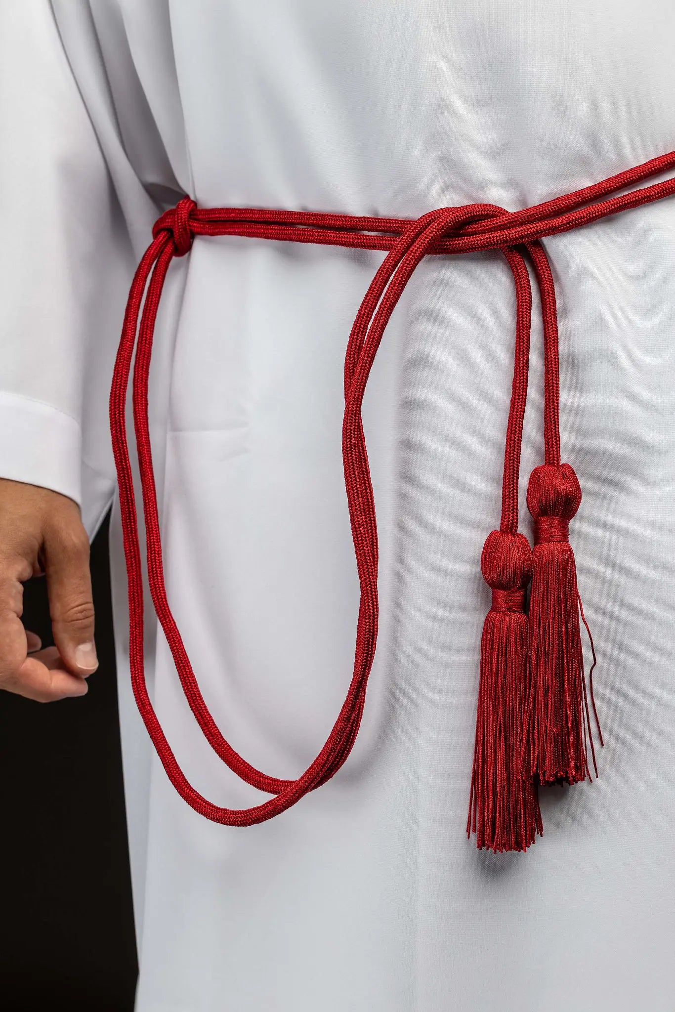 Red liturgical cincture with decorative tassels made from braided cord, tied around an alb.