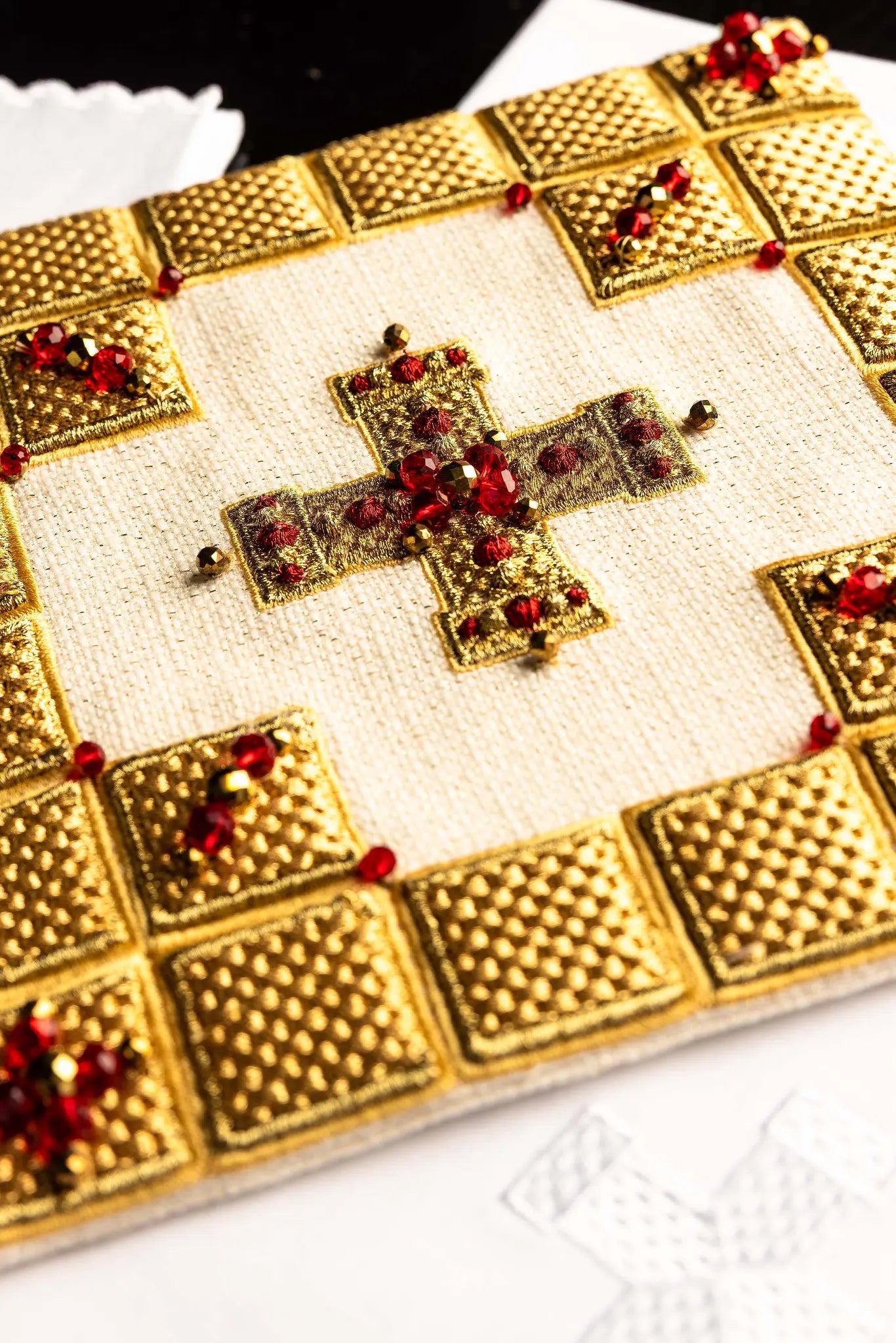 Ecru handmade chalice linen set with a pall featuring a dimensional gold cross, red hematite, and shimmering crystals, a corporal with a central cross, and a purificator and lavabo towel with embroidered crosses, all with scalloped edges.
