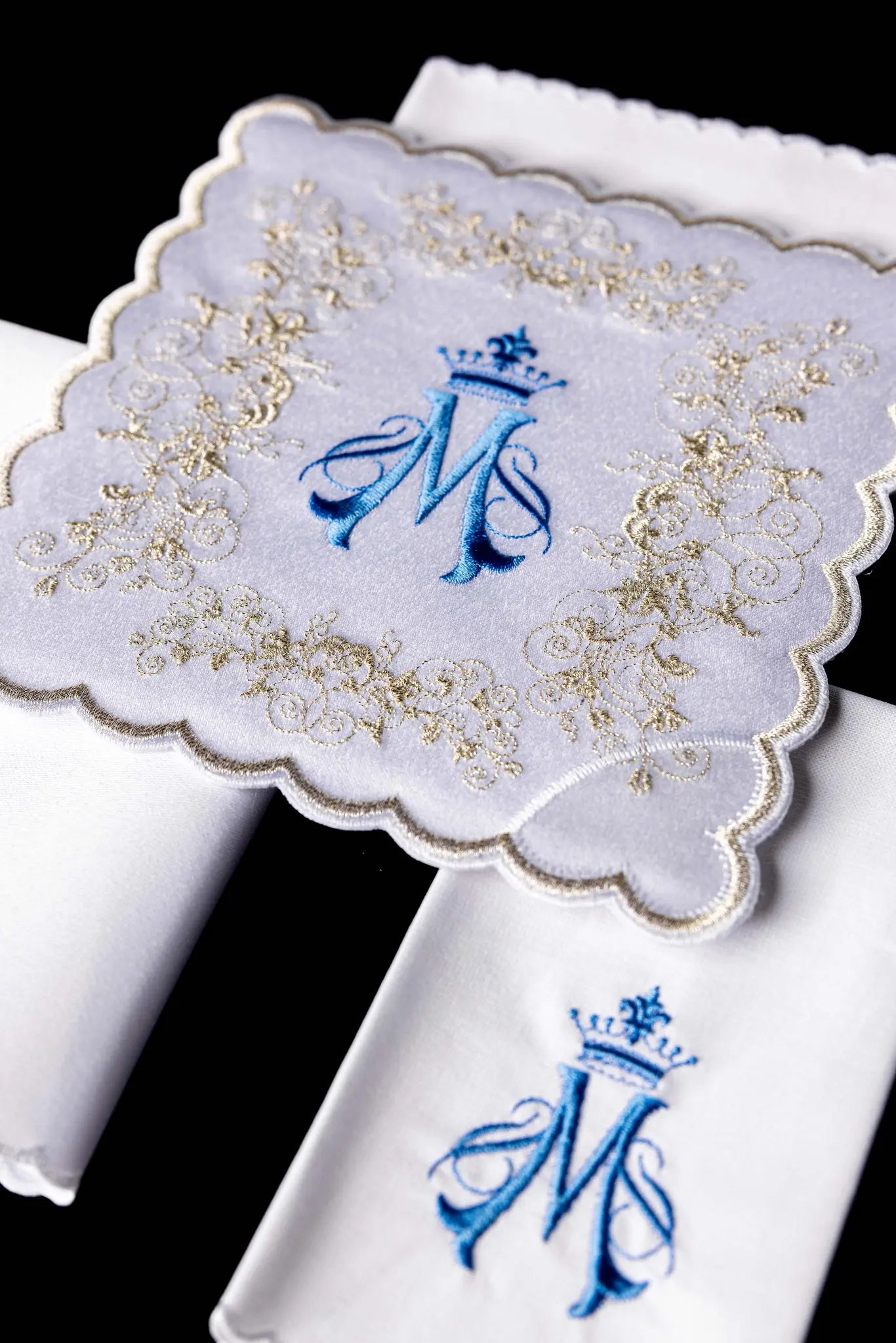 White chalice linen set with Marian monogram embroidery in blue and gold, including pall, corporal, purificator, and lavabo towel.