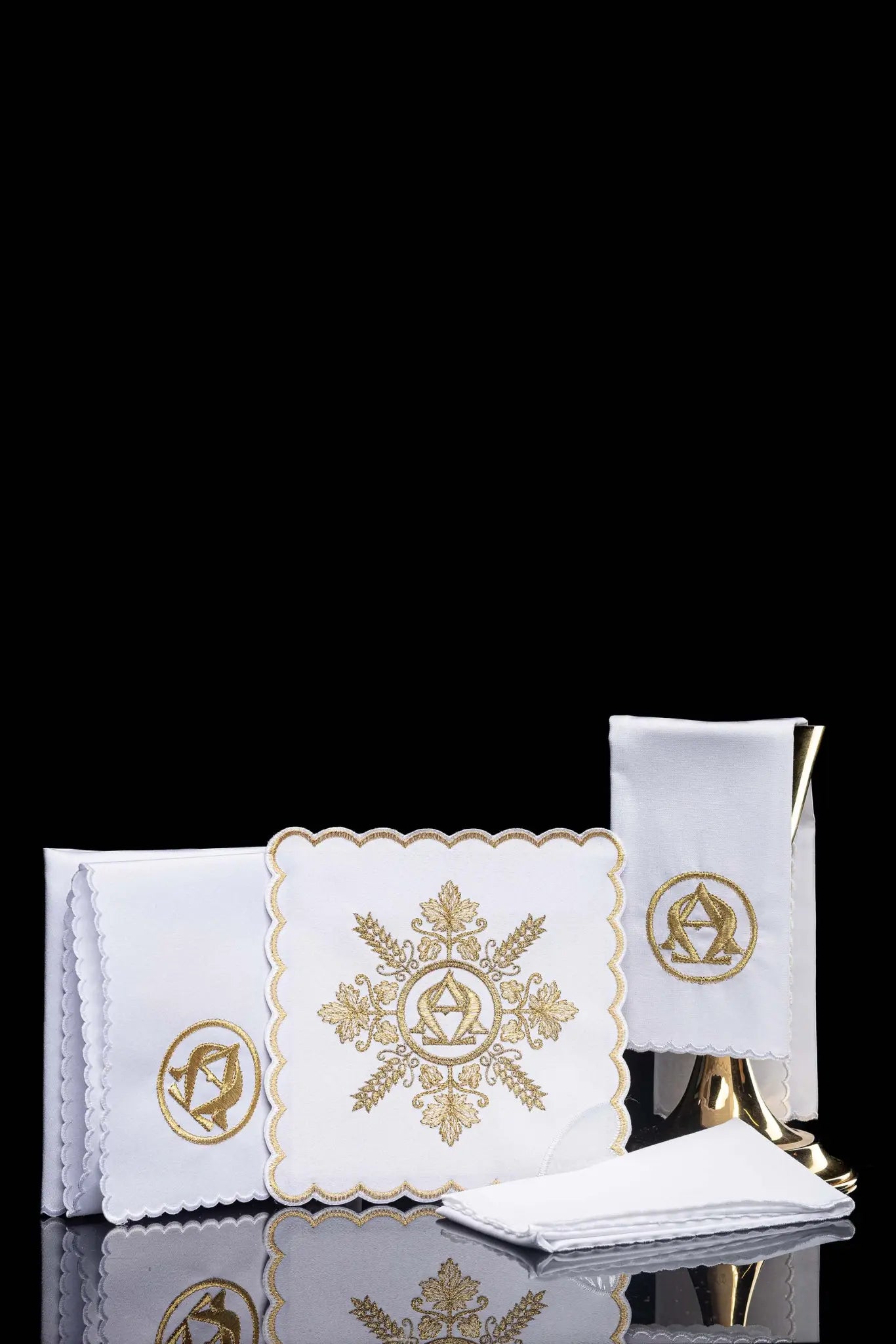 White chalice linen set with gold Alpha and Omega embroidery, including pall, corporal, purificator, and lavabo towel.