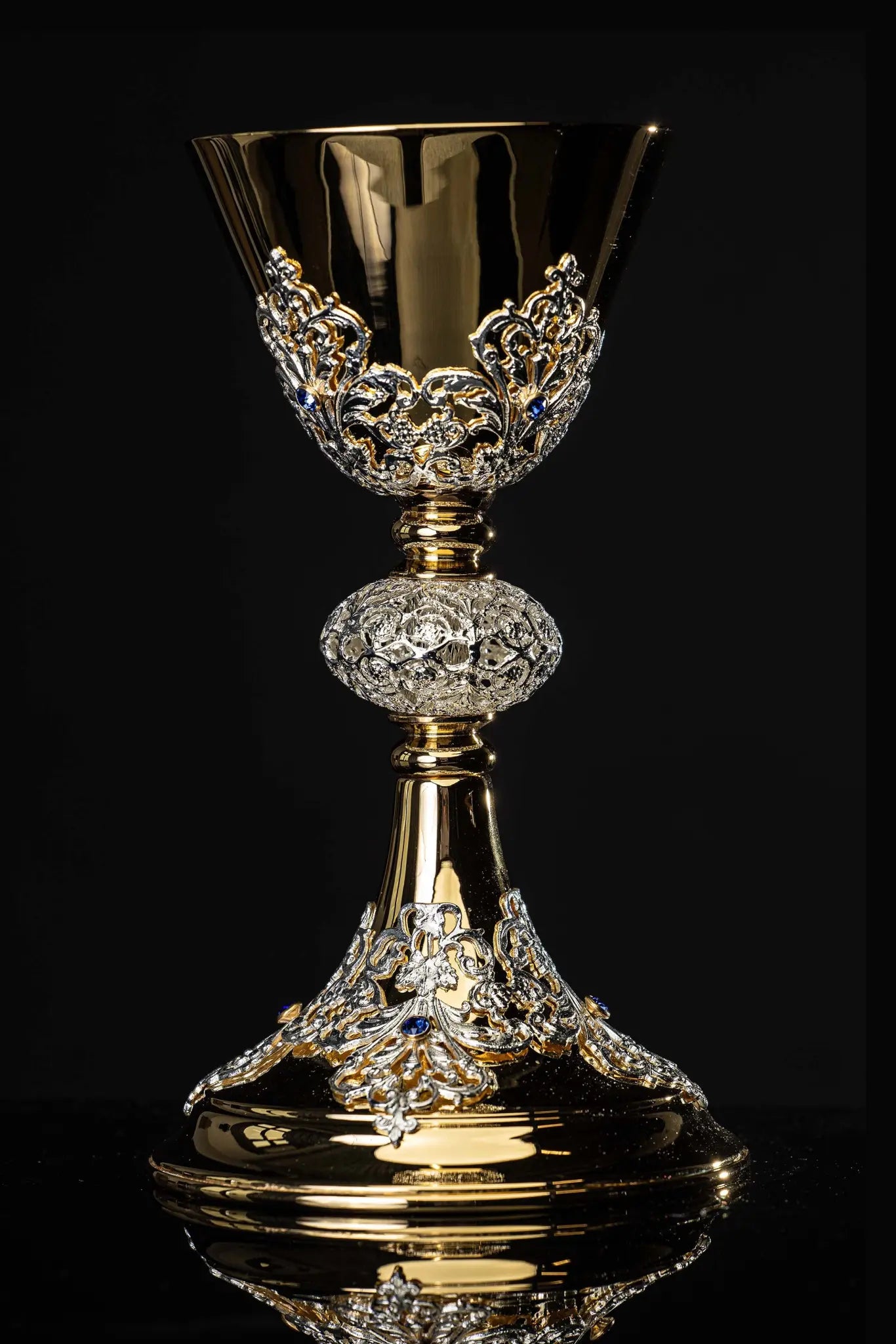 Handmade gold-plated liturgical chalice with silver-plated floral ornamentation and blue sapphire-like stones. The chalice features a decorated cup, nodus, and base.