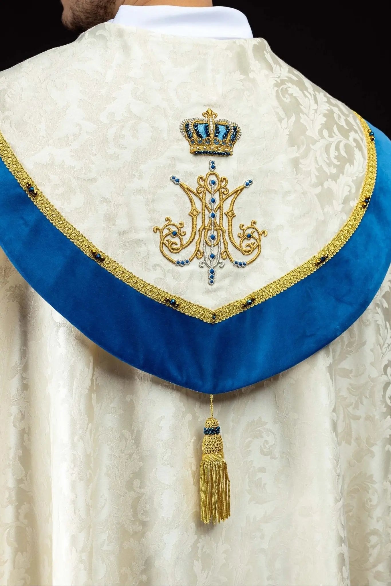 Ecru Marian cope with natural stones and blue velvet trim, part of the Handmade Collection, featuring an ornate metal clasp and gold tassel.