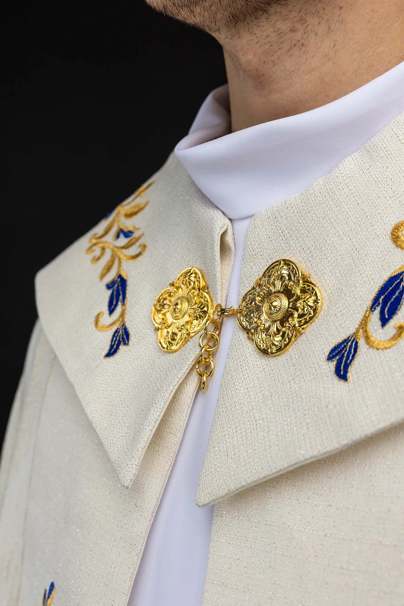 Ecru embroidered cope with Marian symbol, featuring gold and blue floral embroidery, a crowned 'M' monogram, and an ornate gold clasp with chain.
